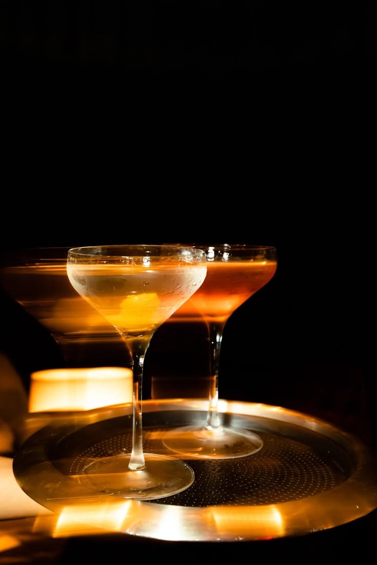 Two coupe glasses on a silver tray in candlelight