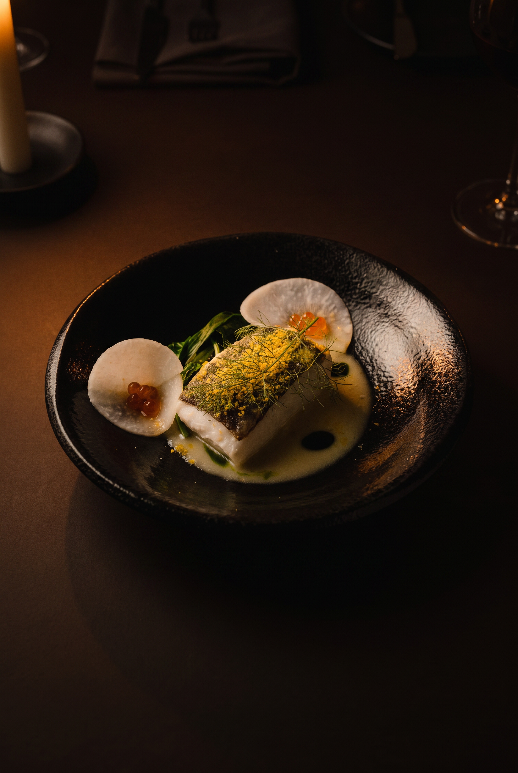 A fish course with fennel and roe in a black bowl
